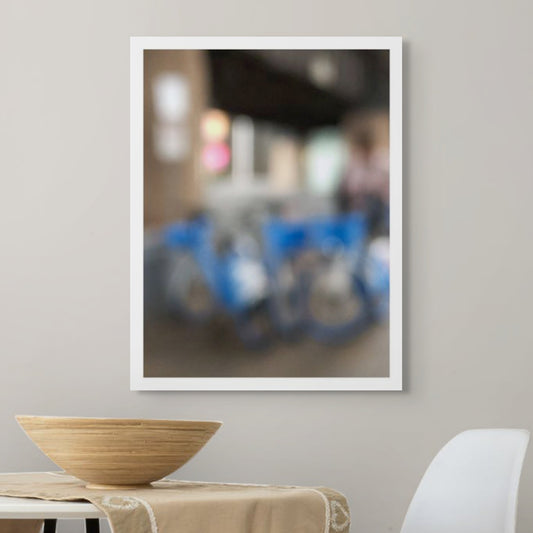 Urban Commute - Series No.1: 9646v1 - Room View, a soft focus image of a group of blue city e-bikes parked in a cluster, with blurred lights and architecture in the background. A passing figure adds motion to the scene. Limited edition fine art print by Raymond Mather.