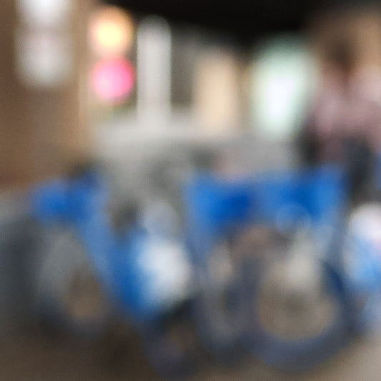 Urban Commute - Series No.1: 9646v1 - Close Detail View, a soft focus image of a group of blue city e-bikes parked in a cluster, with blurred lights and architecture in the background. A passing figure adds motion to the scene. Limited edition fine art print by Raymond Mather.