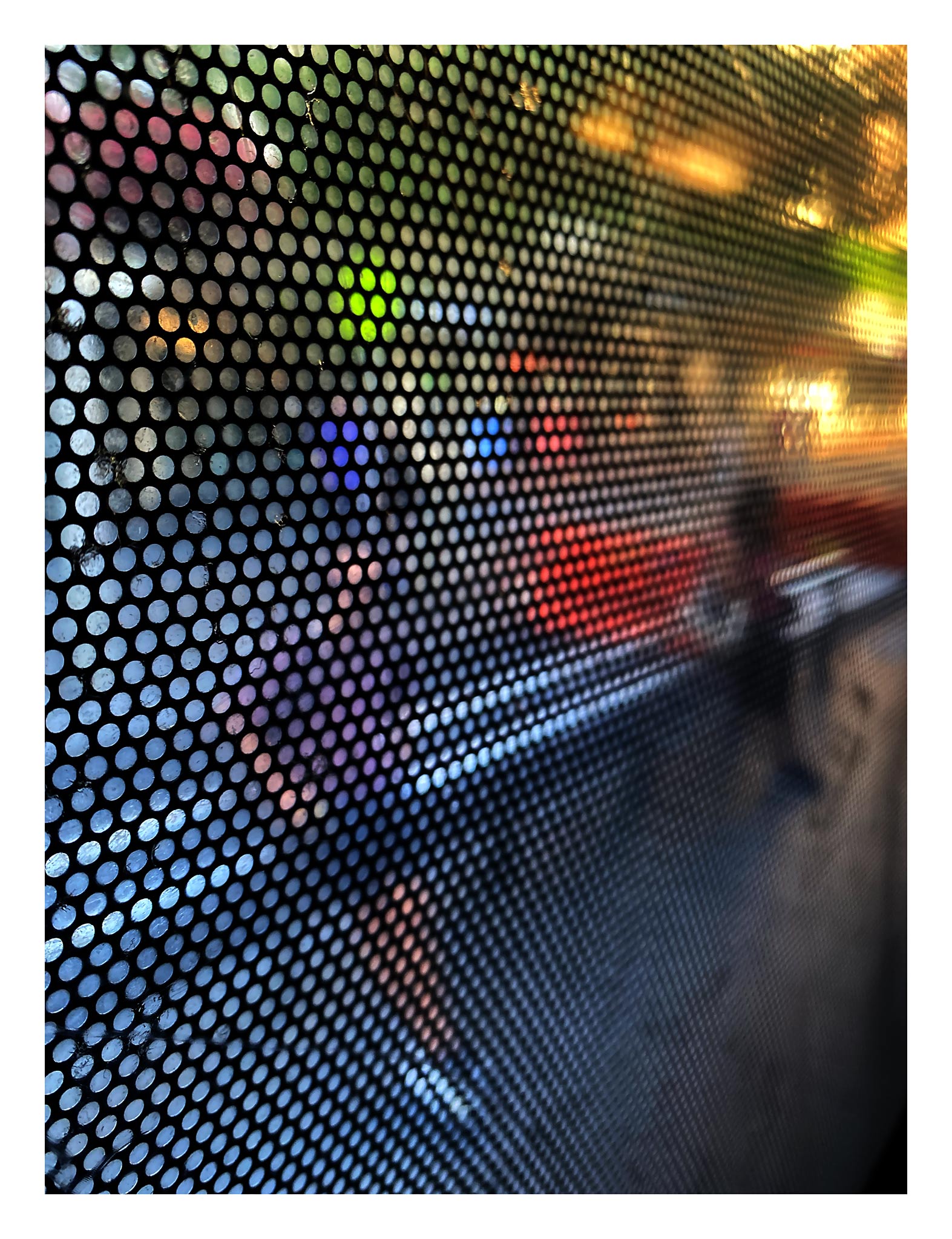 Urban Commute - Series No.2: 0785 - 81.5x104cm, fine art photograph by Raymond Mather featuring a blurred pedestrian viewed through a perforated window screen. Vibrant colours of red, purple, and green shimmer across the gridded surface, creating a dynamic abstract portrait of city life in motion.