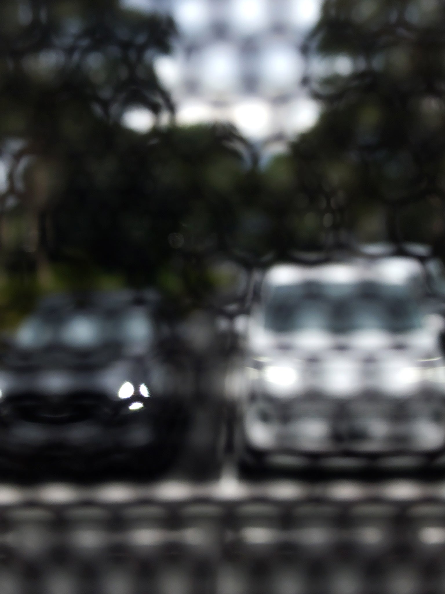 Urban Commute - Series No.2: 8468(1)v1 - 67.5x90cm, fine art photograph by Raymond Mather featuring a soft-focus image of two parked cars, one dark, one white, viewed through a textured, patterned screen. The effect blurs details and creates a moody, abstract urban vignette rich in contrast and stillness.