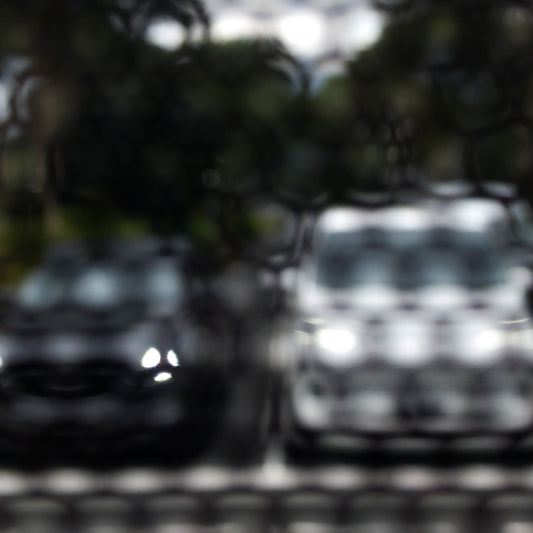 Urban Commute - Series No.2: 8468(1)v1 - Close Detail View, fine art photograph by Raymond Mather featuring a soft-focus image of two parked cars, one dark, one white, viewed through a textured, patterned screen. The effect blurs details and creates a moody, abstract urban vignette rich in contrast and stillness.