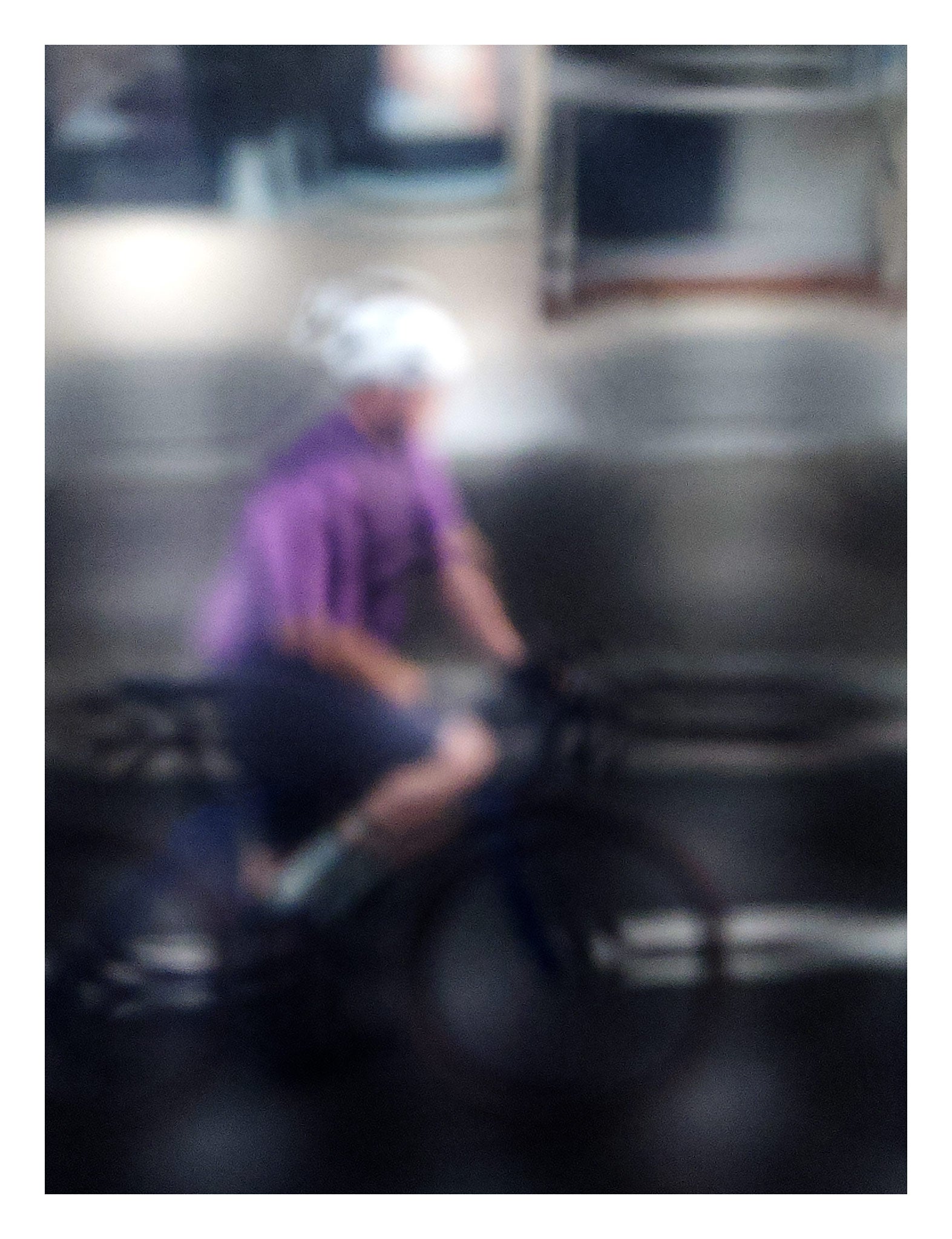 Urban Commute, Series No.2: 8621(1)v1 - 81.5x104cm, fine art photograph by Raymond Mather featuring a blurred cyclist in purple shirt and white helmet, riding through a moody, reflective cityscape. The image is softly distorted, blending motion with atmosphere in a dreamlike urban abstraction.