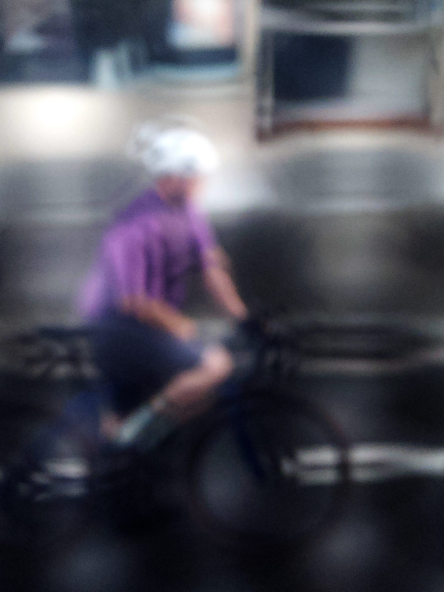 Urban Commute, Series No.2: 8621(1)v1 - 67.5x90cm, fine art photograph by Raymond Mather featuring a blurred cyclist in purple shirt and white helmet, riding through a moody, reflective cityscape. The image is softly distorted, blending motion with atmosphere in a dreamlike urban abstraction.