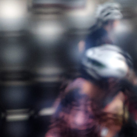 Urban Commute - Series No.2: 8622(1) - Close Detail View, fine art photograph by Raymond Mather featuring two blurred cyclists in motion, seen through a diffused surface. The image blends pink, navy, and silver tones into an abstract composition of rhythm, reflection, and fleeting urban energy.