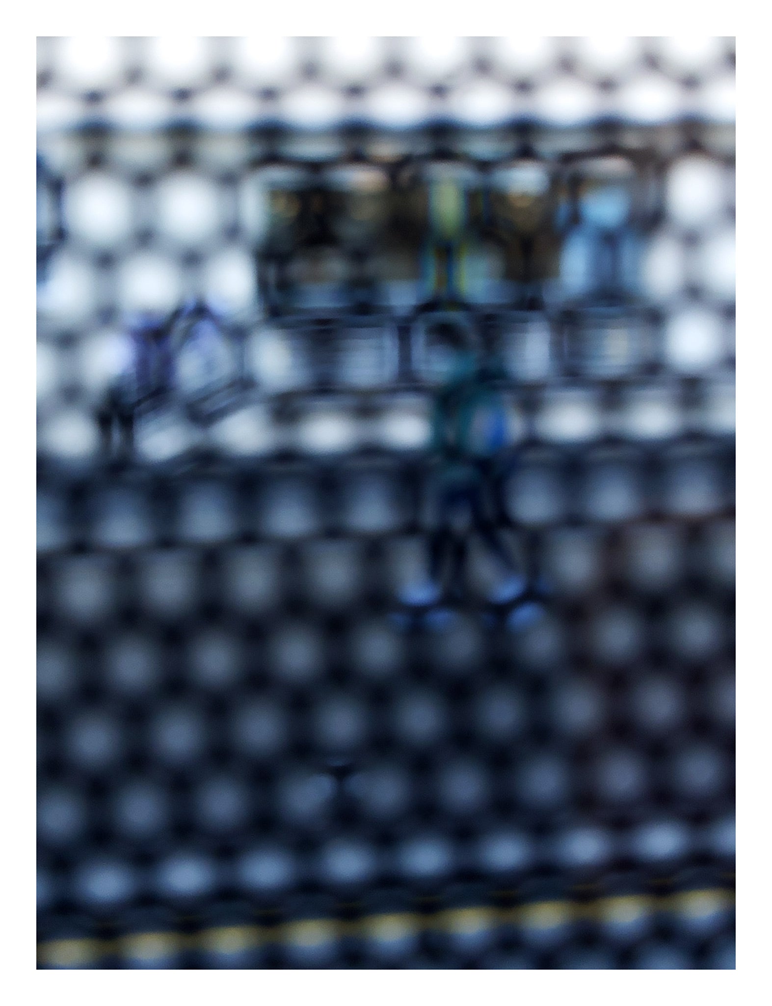 Urban Commute - Series No.2: 9150 - 81.5x104cm, fine art photograph by Raymond Mather showing a walking figure in blue, captured through a dense circular grid. A blurred train forms the backdrop, creating a quiet, geometric abstraction of city life in motion.
