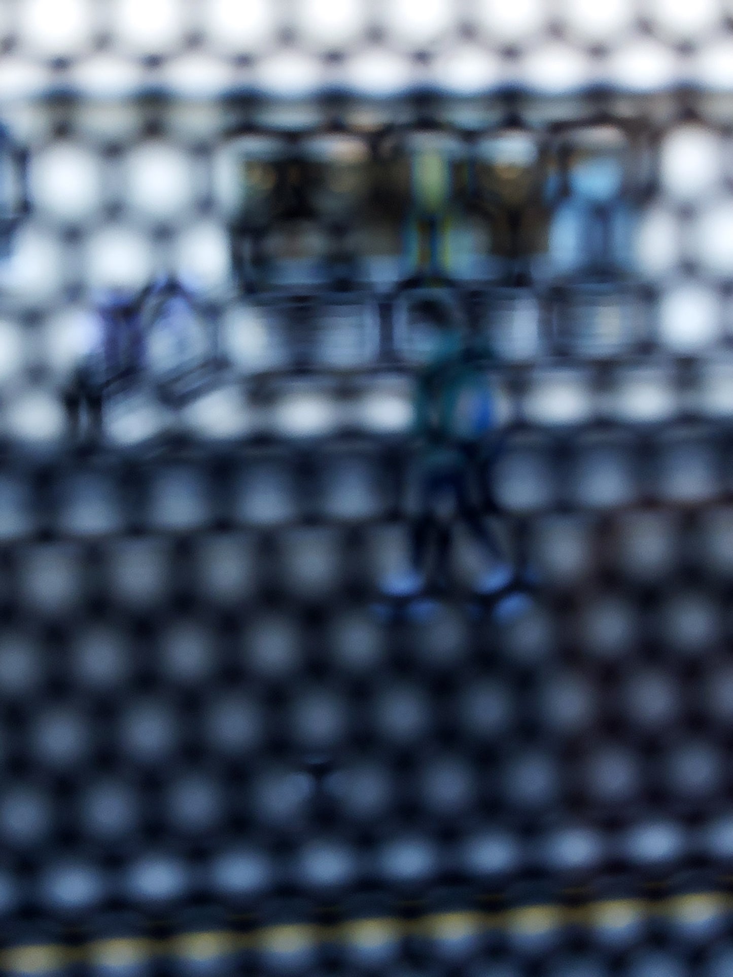 Urban Commute - Series No.2: 9150 - 67.5x90cm, fine art photograph by Raymond Mather showing a walking figure in blue, captured through a dense circular grid. A blurred train forms the backdrop, creating a quiet, geometric abstraction of city life in motion.
