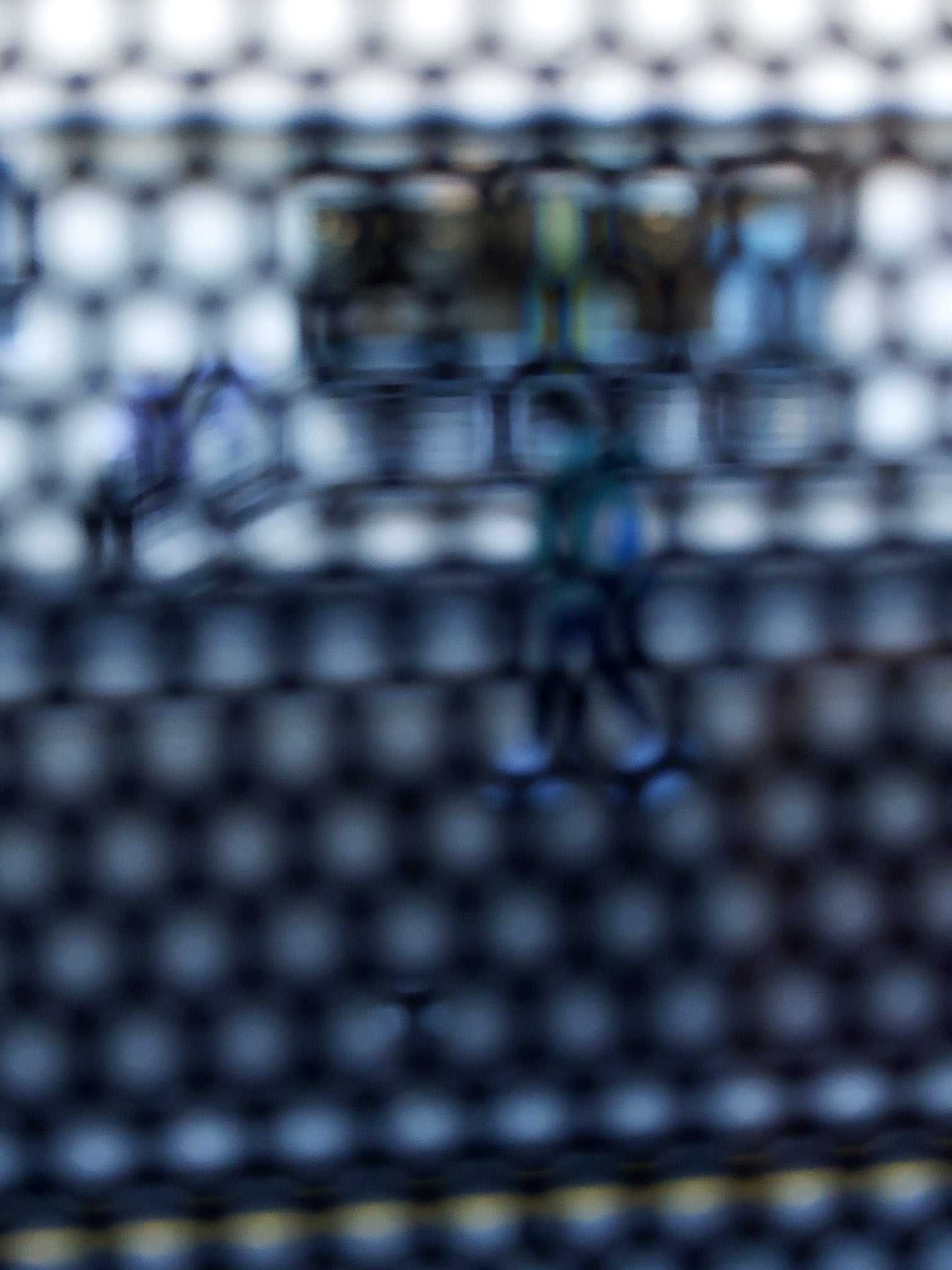 Urban Commute - Series No.2: 9150 - 67.5x90cm, fine art photograph by Raymond Mather showing a walking figure in blue, captured through a dense circular grid. A blurred train forms the backdrop, creating a quiet, geometric abstraction of city life in motion.