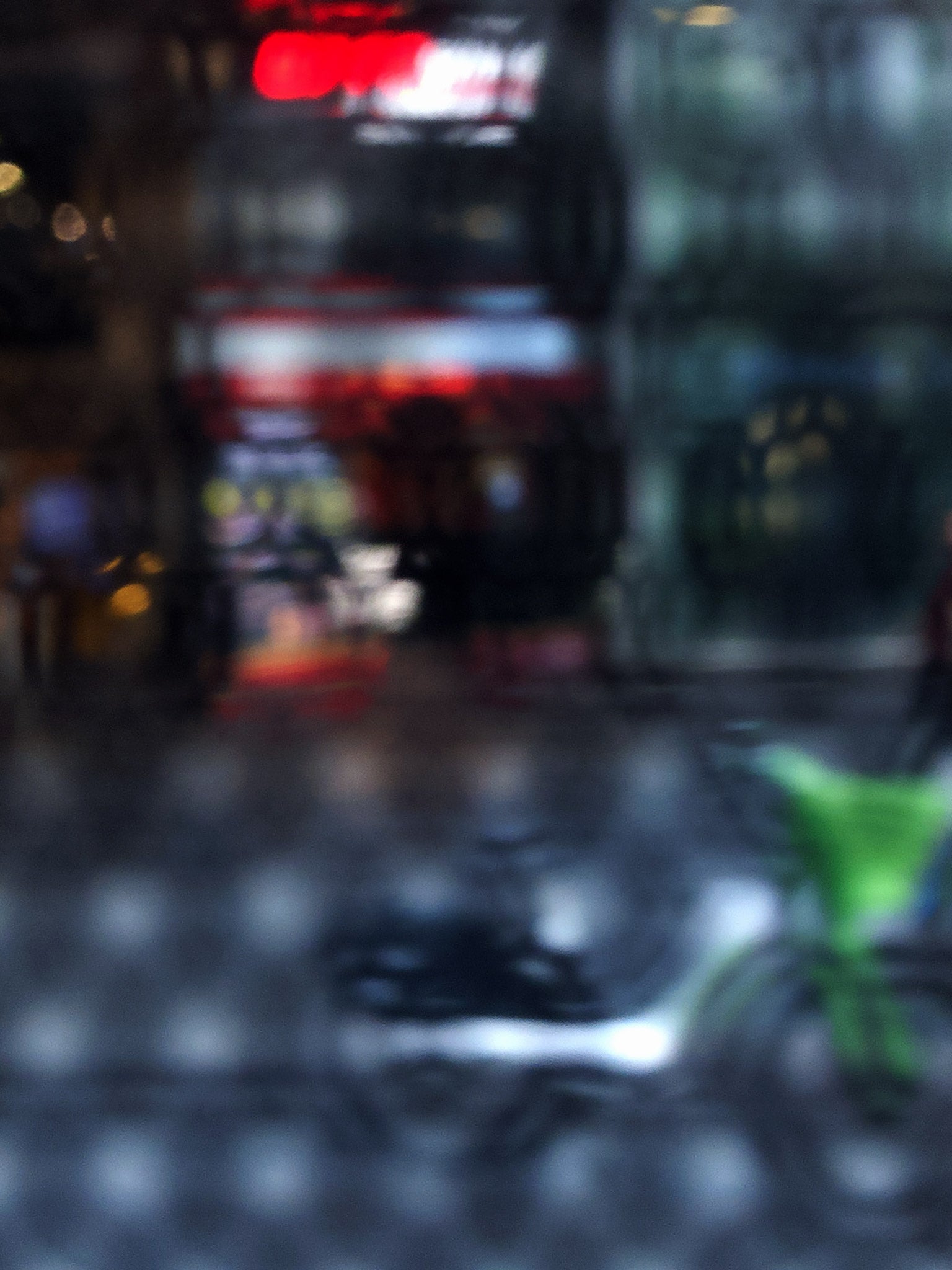 Urban Commute - Series No.2: 9206v1 - 67.5x90cm, fine art photograph by Raymond Mather featuring a blurred green bike in the foreground, with a red neon-lit storefront behind a softly distorted surface. A moody and abstract urban scene evoking energy and reflection.
