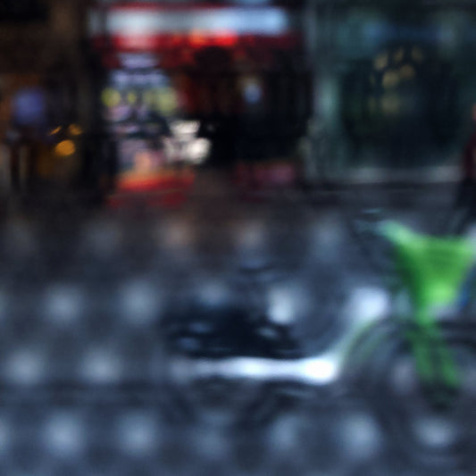 Urban Commute - Series No.2: 9206v1 - Close Detail View, fine art photograph by Raymond Mather featuring a blurred green bike in the foreground, with a red neon-lit storefront behind a softly distorted surface. A moody and abstract urban scene evoking energy and reflection.