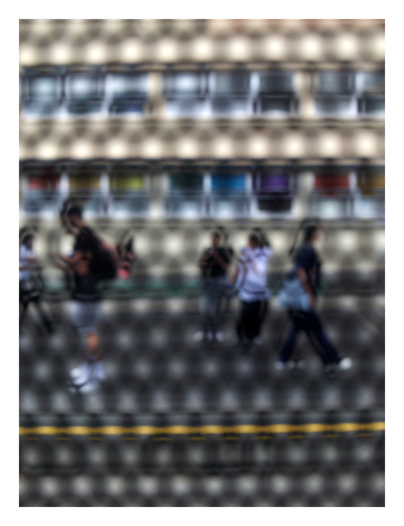 Urban Commute - Series No.2: 9558(1)v1 - 81.5x104cm, fine art photograph by Raymond Mather showing a group of pedestrians walking past a multicoloured glass façade, viewed through a circular screen. The image blurs motion, structure, and rhythm into a poetic urban abstraction.