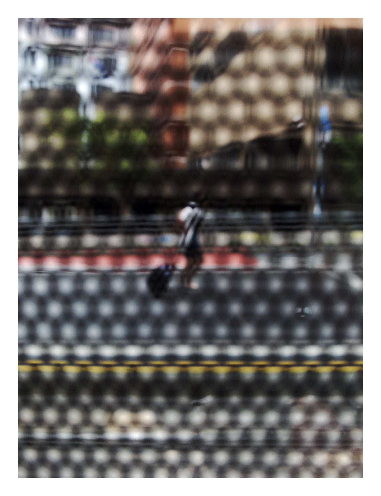 Urban Commute - Series No.2: 9569(1)v1 - 81.5x104cm, fine art photograph by Raymond Mather featuring a lone blurred figure walking along a city street. Viewed through a dotted screen, the image blends red kerb, yellow line, and soft building reflections into a textured urban abstraction.