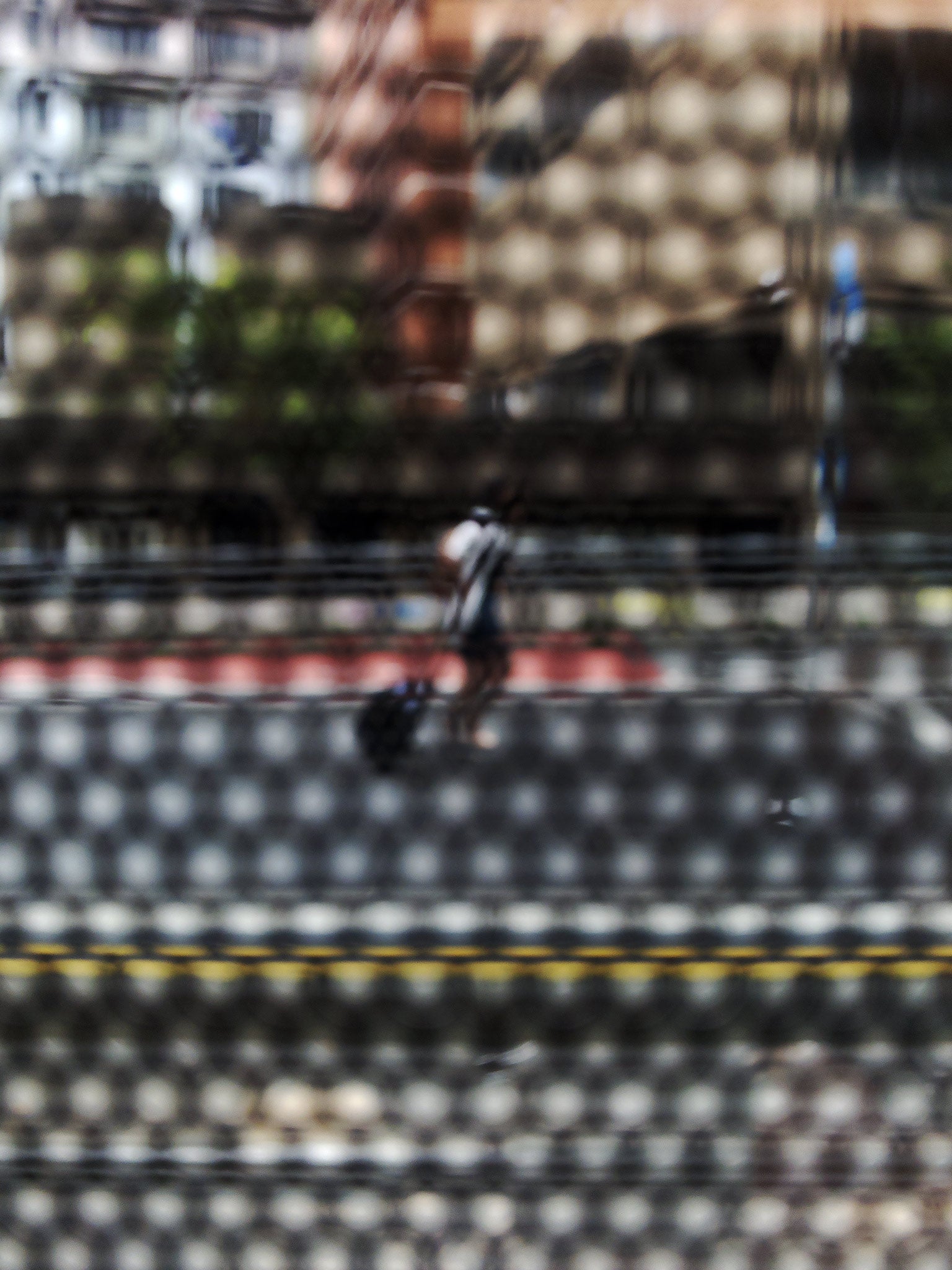 Urban Commute - Series No.2: 9569(1)v1 - 67.5x90cm, fine art photograph by Raymond Mather featuring a lone blurred figure walking along a city street. Viewed through a dotted screen, the image blends red kerb, yellow line, and soft building reflections into a textured urban abstraction.
