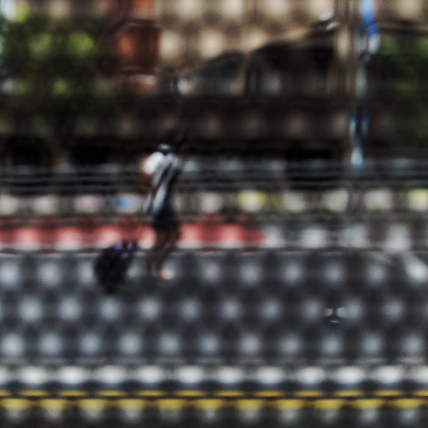 Urban Commute - Series No.2: 9569(1)v1 - Close Detail View, fine art photograph by Raymond Mather featuring a lone blurred figure walking along a city street. Viewed through a dotted screen, the image blends red kerb, yellow line, and soft building reflections into a textured urban abstraction.