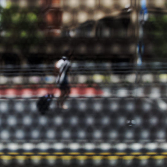 Urban Commute - Series No.2: 9569(1)v1 - Close Detail View, fine art photograph by Raymond Mather featuring a lone blurred figure walking along a city street. Viewed through a dotted screen, the image blends red kerb, yellow line, and soft building reflections into a textured urban abstraction.