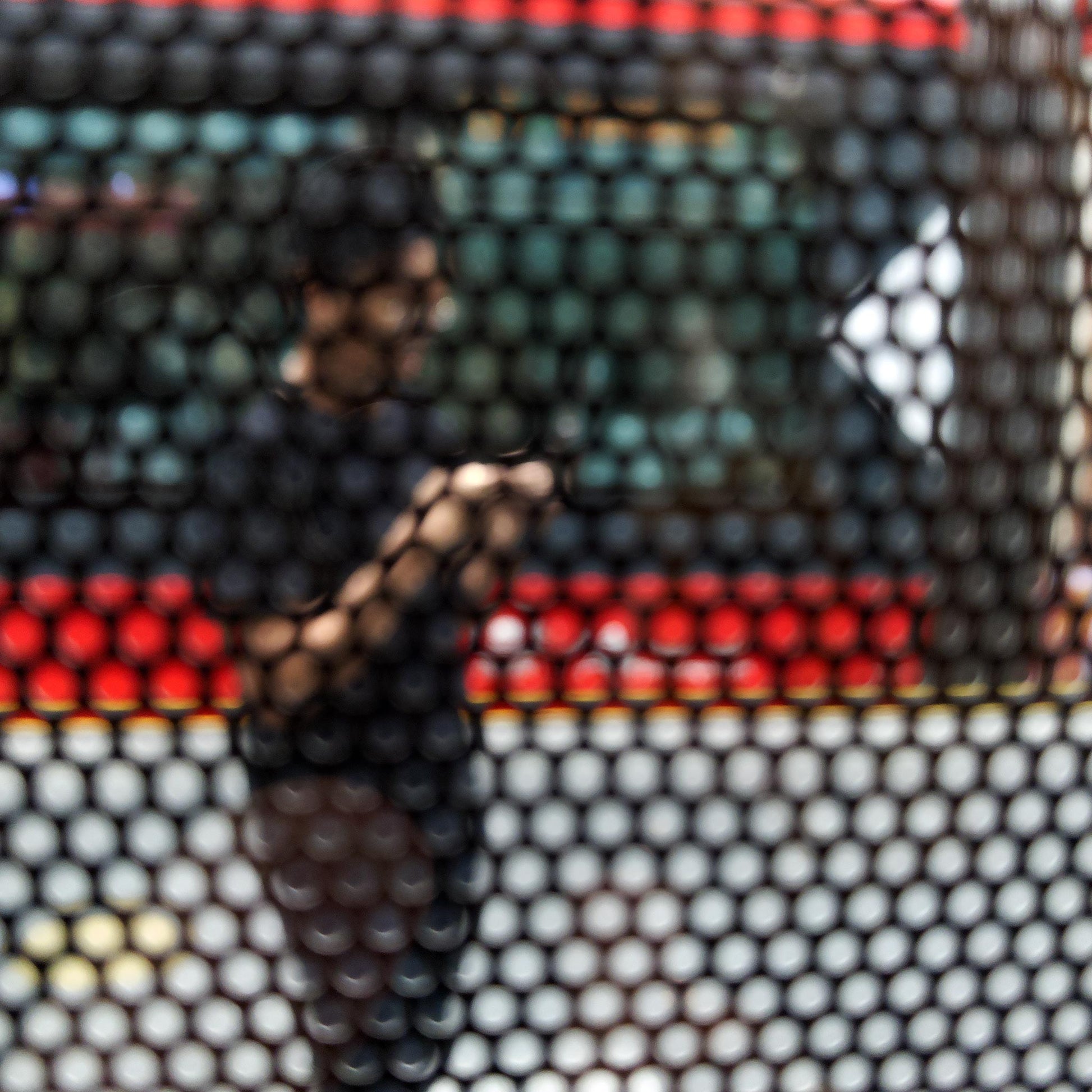 Urban Commute - Series No.2: 9574(1)v1 - Close Detail View, fine art photograph by Raymond Mather featuring a blurred figure using a phone, seen through a patterned screen with a red and green bus in the background. A richly layered urban image exploring distraction, movement, and modern life.