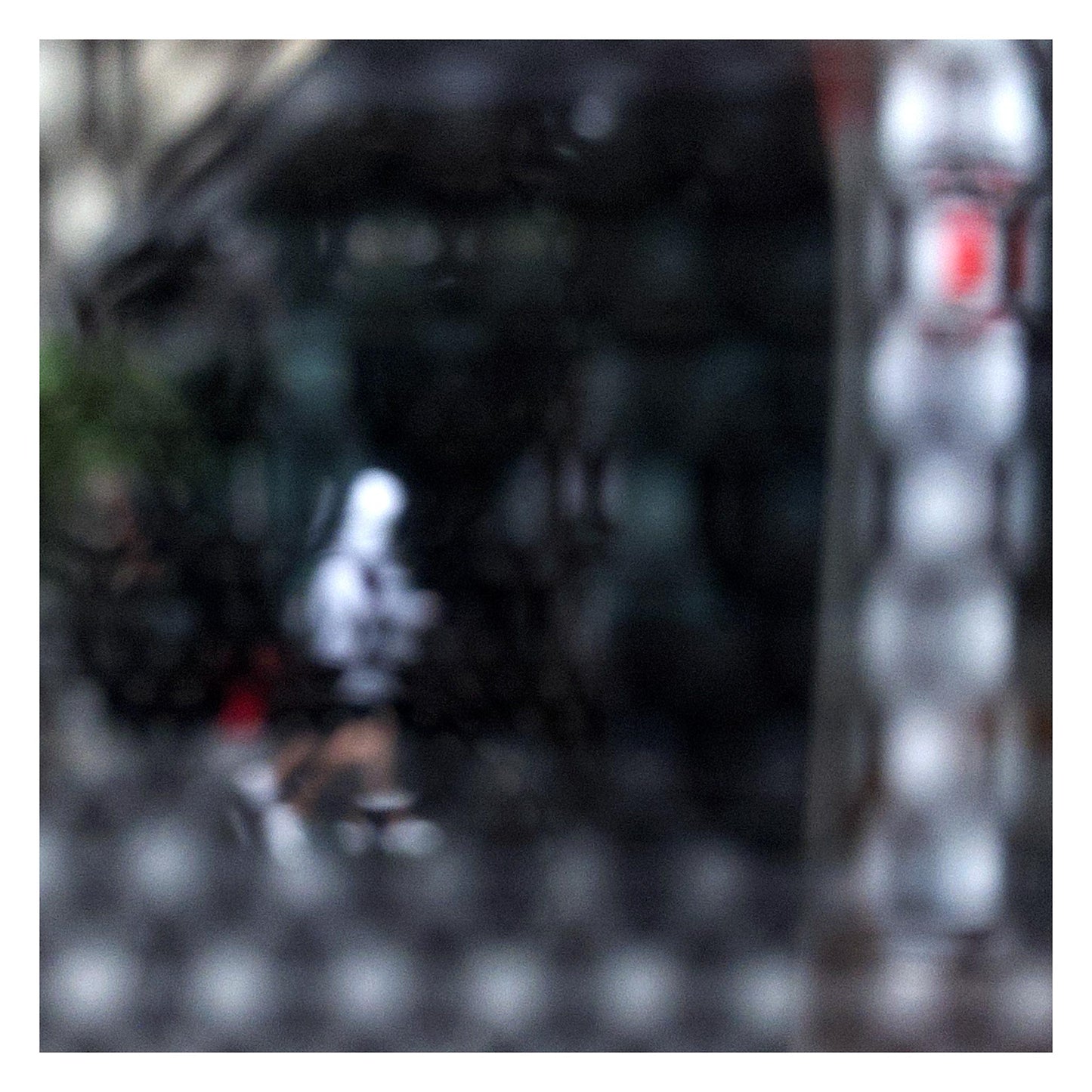 Urban Commute - Series No.2: 9590v1 - 104x104cm, fine art photograph by Raymond Mather showing a blurred white-hooded figure walking across a dark city street, seen through a patterned screen. A haunting study in motion, texture, and introspection.