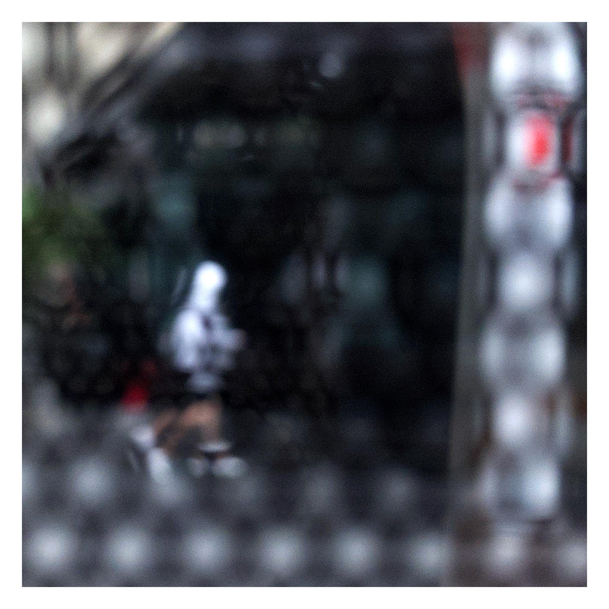 Urban Commute - Series No.2: 9590v1 - 104x104cm, fine art photograph by Raymond Mather showing a blurred white-hooded figure walking across a dark city street, seen through a patterned screen. A haunting study in motion, texture, and introspection.