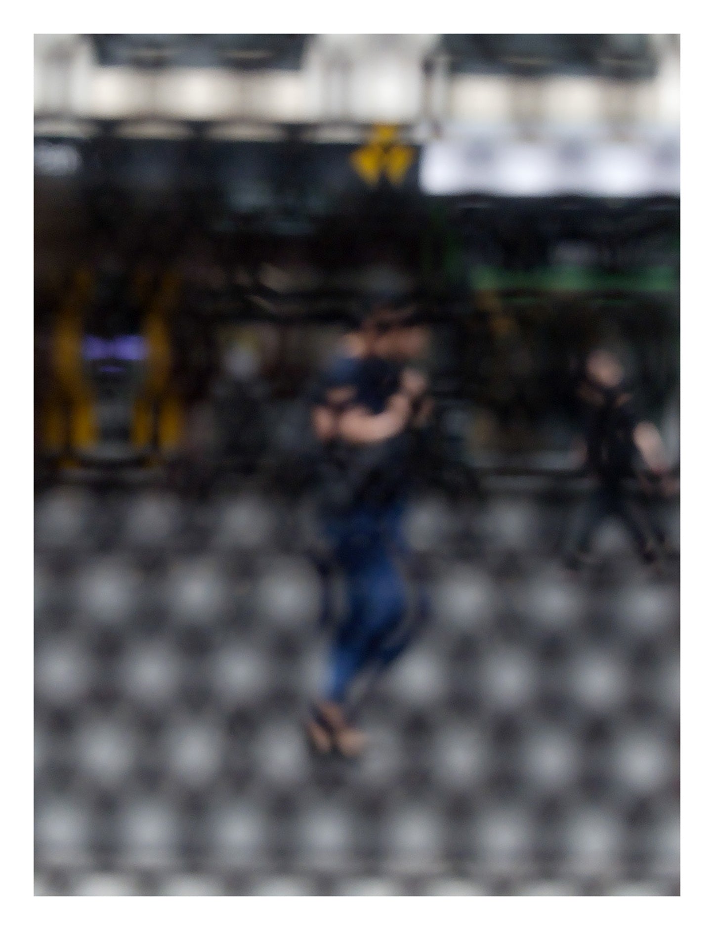 Urban Commute - Series No.2: 9609 - 81.5x104cm, fine art photograph by Raymond Mather featuring a blurred morning commuter with a backpack, seen mid-stride through a patterned surface. Another figure passes in the background. A layered urban image of movement and solitude.