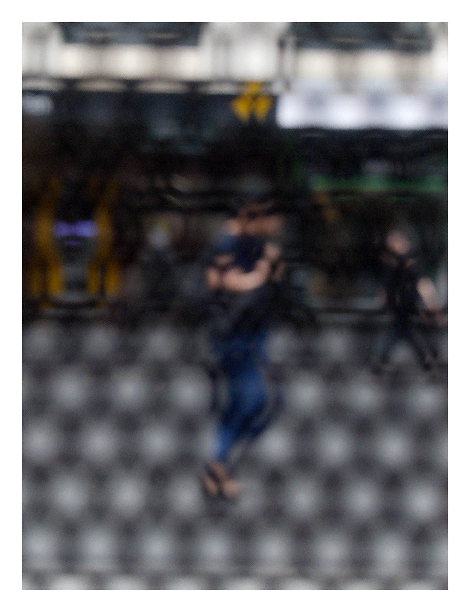 Urban Commute - Series No.2: 9609 - 81.5x104cm, fine art photograph by Raymond Mather featuring a blurred morning commuter with a backpack, seen mid-stride through a patterned surface. Another figure passes in the background. A layered urban image of movement and solitude.