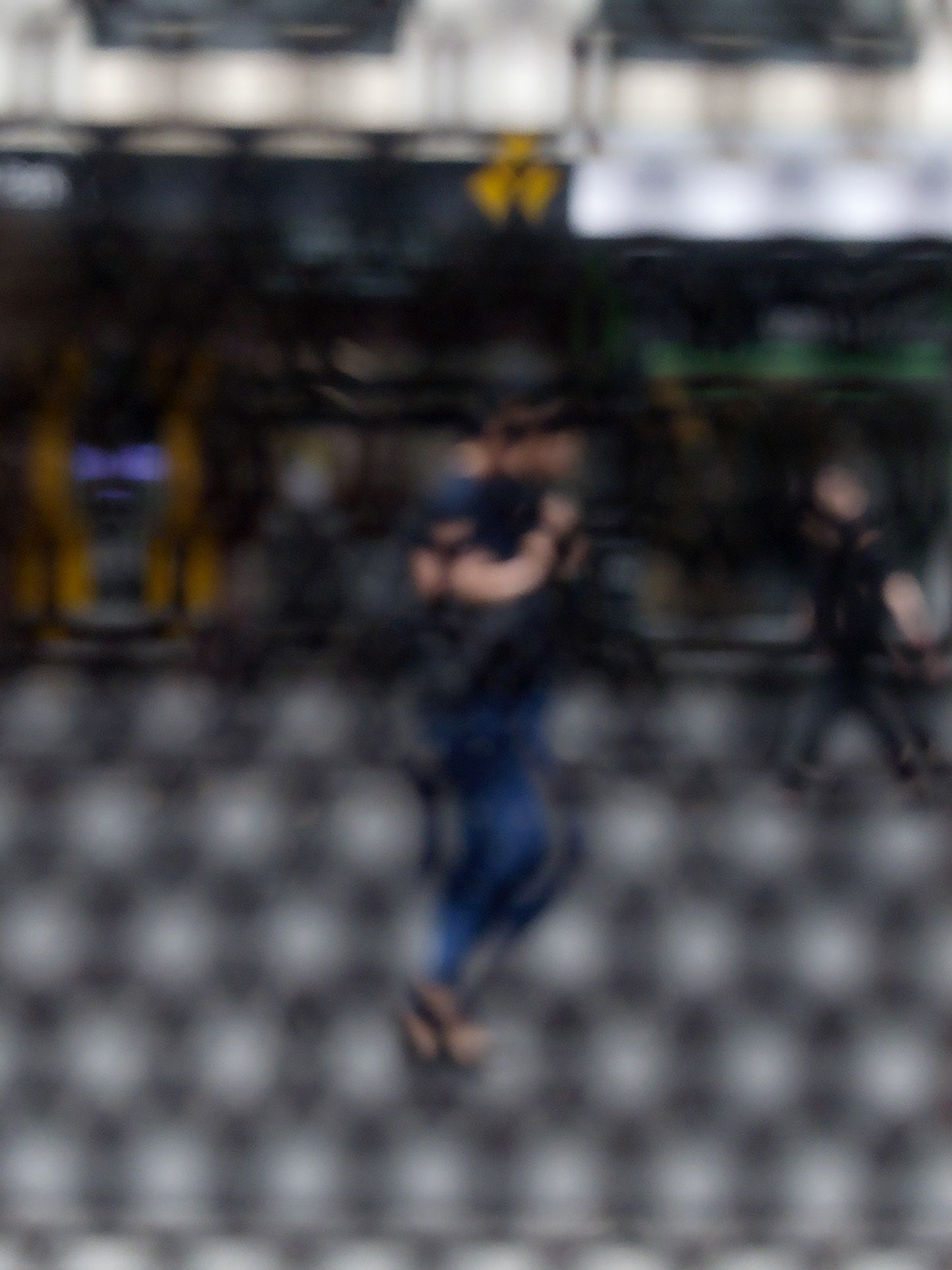 Urban Commute - Series No.2: 9609 - 67.5x90cm, fine art photograph by Raymond Mather featuring a blurred morning commuter with a backpack, seen mid-stride through a patterned surface. Another figure passes in the background. A layered urban image of movement and solitude.